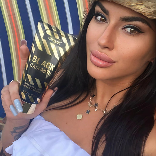 Frau mit dunklem Haar hält Onyx Black Cashmere Bräunungscreme in der Hand, goldene Verpackung glänzt im Sonnenlicht