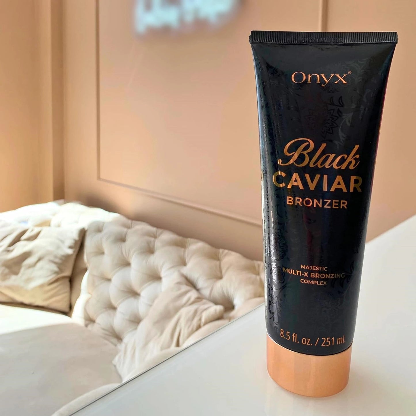 Blonde Frau mit sichtbaren Tattoos haelt Onyx Black Caviar Braunungslotion 251ml im Wohnzimmer mit Fensterlicht