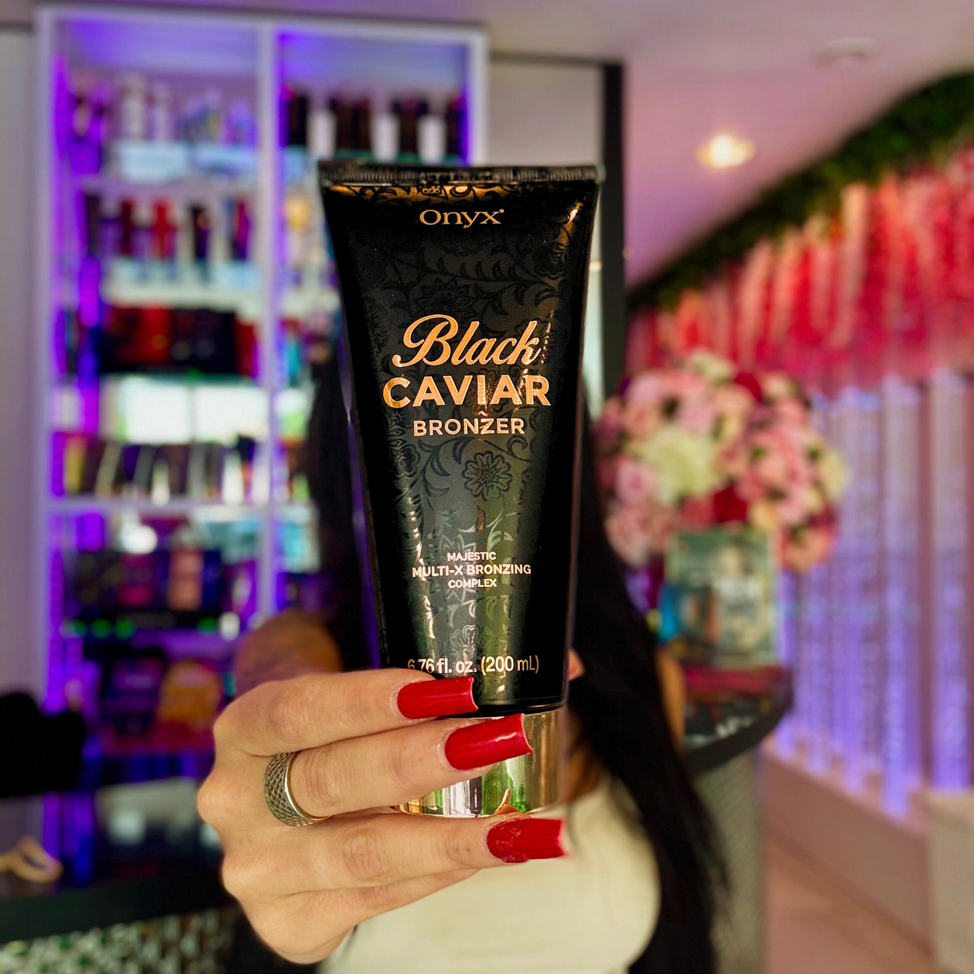 Frau hält die Onyx Black Caviar Lotion 251ml vor cremefarbener Wand und Sofa mit dezentem Lichtspiel im Hintergrund