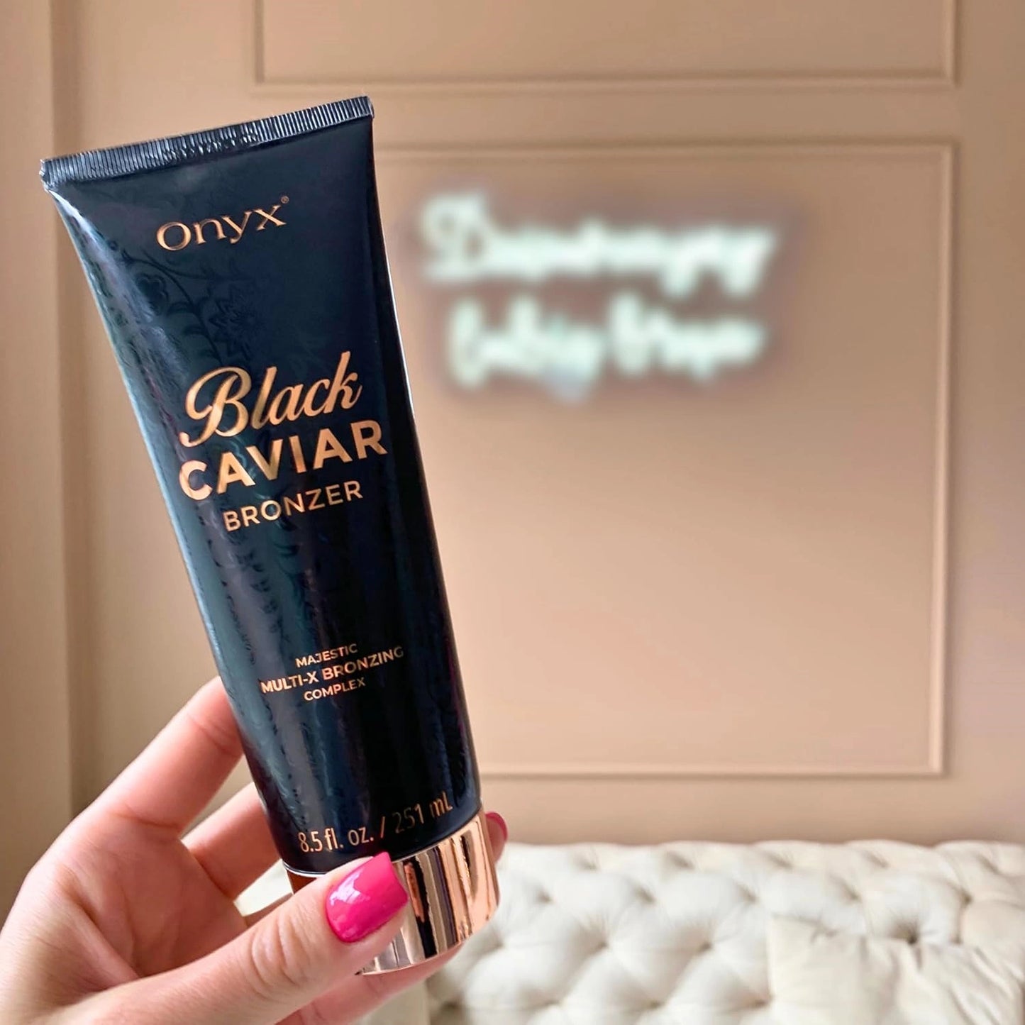Onyx Black Caviar Bräunungslotion 251ml wird in der Hand einer Frau im Solarium mit lila und pinkem Licht gehalten