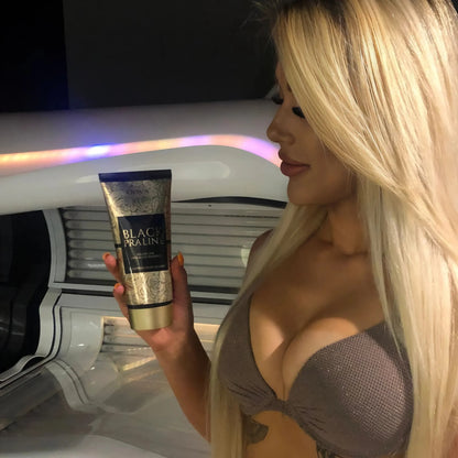 Blonde Frau mit langen Haaren hält Onyx Black Praline Lotion vor Solarium und schaut darauf