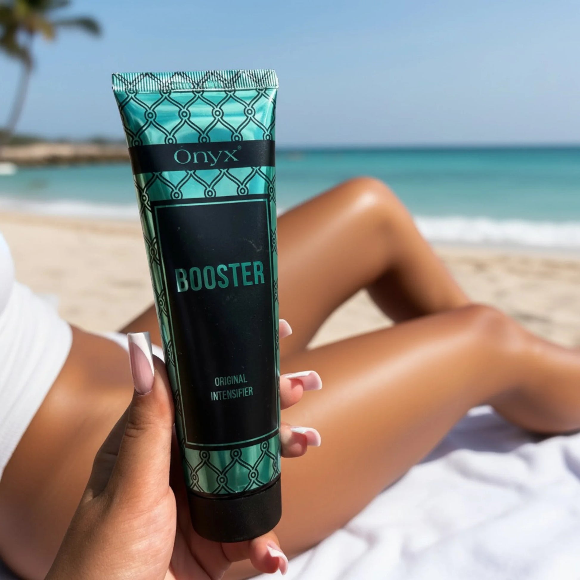 Onyx Booster Bräunungsintensivierer wird vor einem sonnigen Strand und türkisfarbenem Meer gehalten.