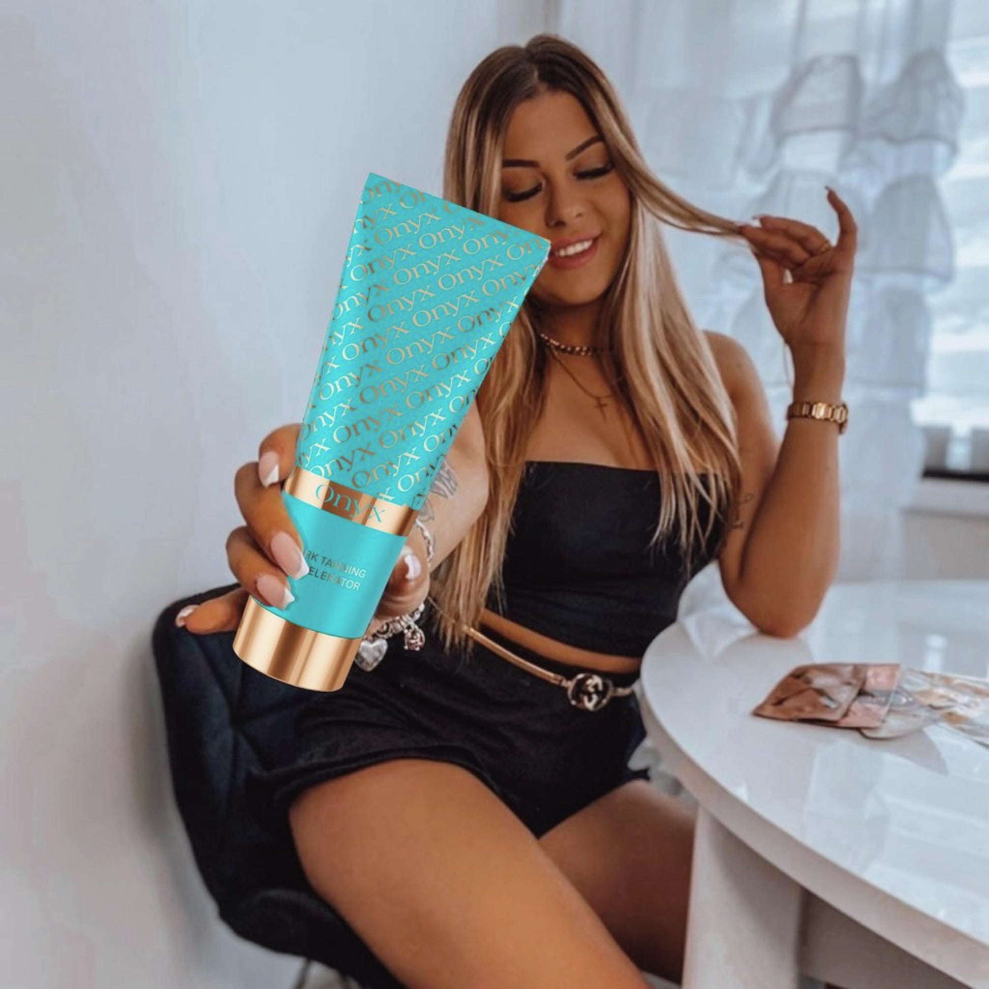 Frau in schwarzem Outfit sitzt am Tisch und hält Onyx Bräunungsbeschleuniger Creme in der Hand