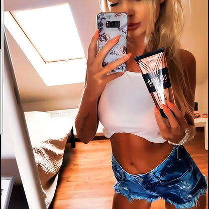 Frau macht Selfie im weißen Top und Jeansshorts, zeigt ihre gebräunte Taille und hält Onyx Grand Cru Bräunungscreme vor dem Spiegel