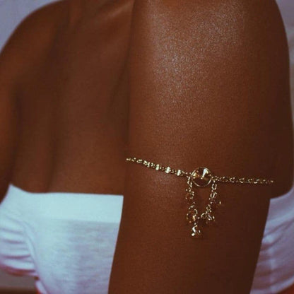 Nahaufnahme von schimmernder gebräunter Haut mit goldener Armkette und weißem Oberteil