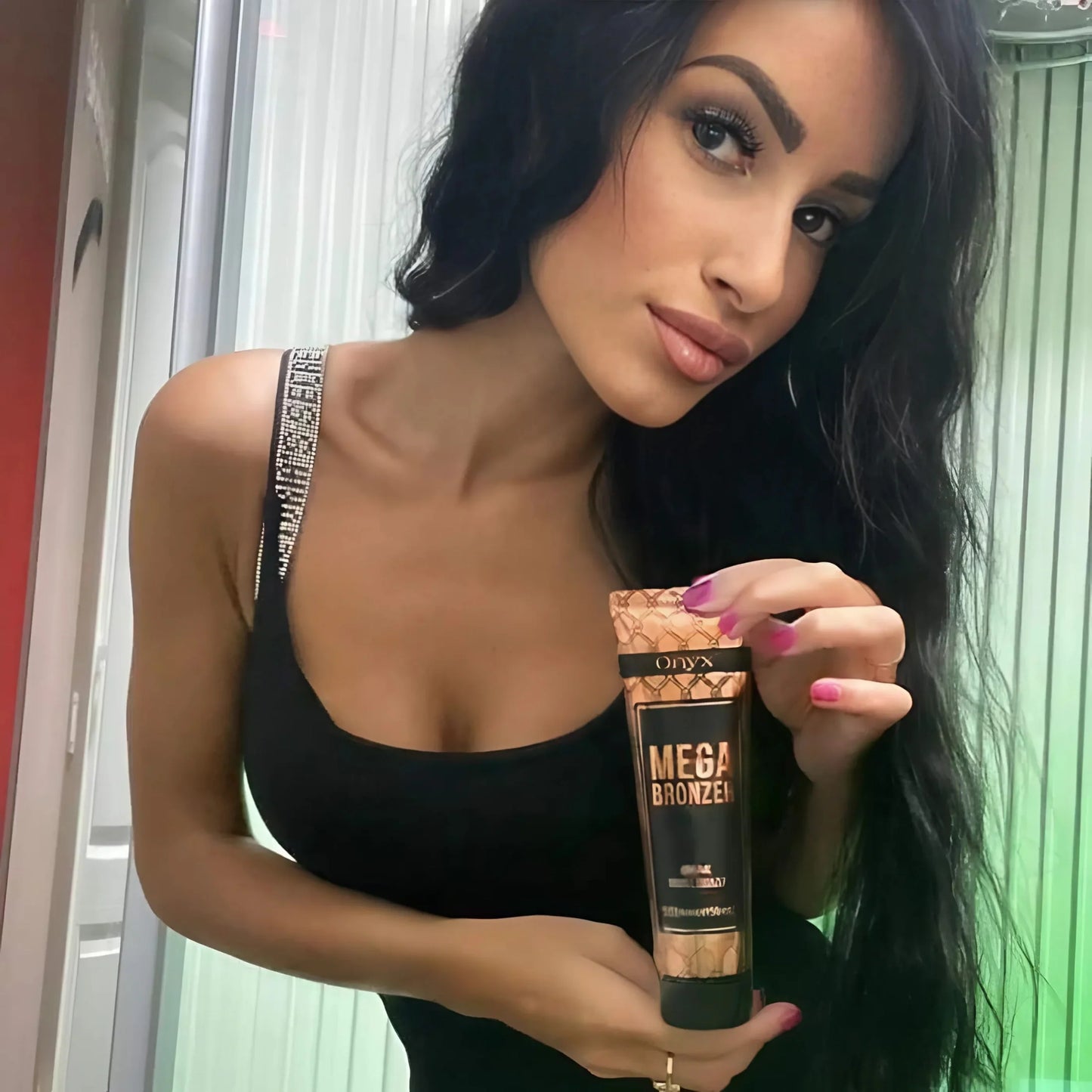 Brünette Frau mit eleganter Ausstrahlung präsentiert Onyx Mega Bronzer vor Solarium, ideal für eine tiefe und gleichmäßige Bräune