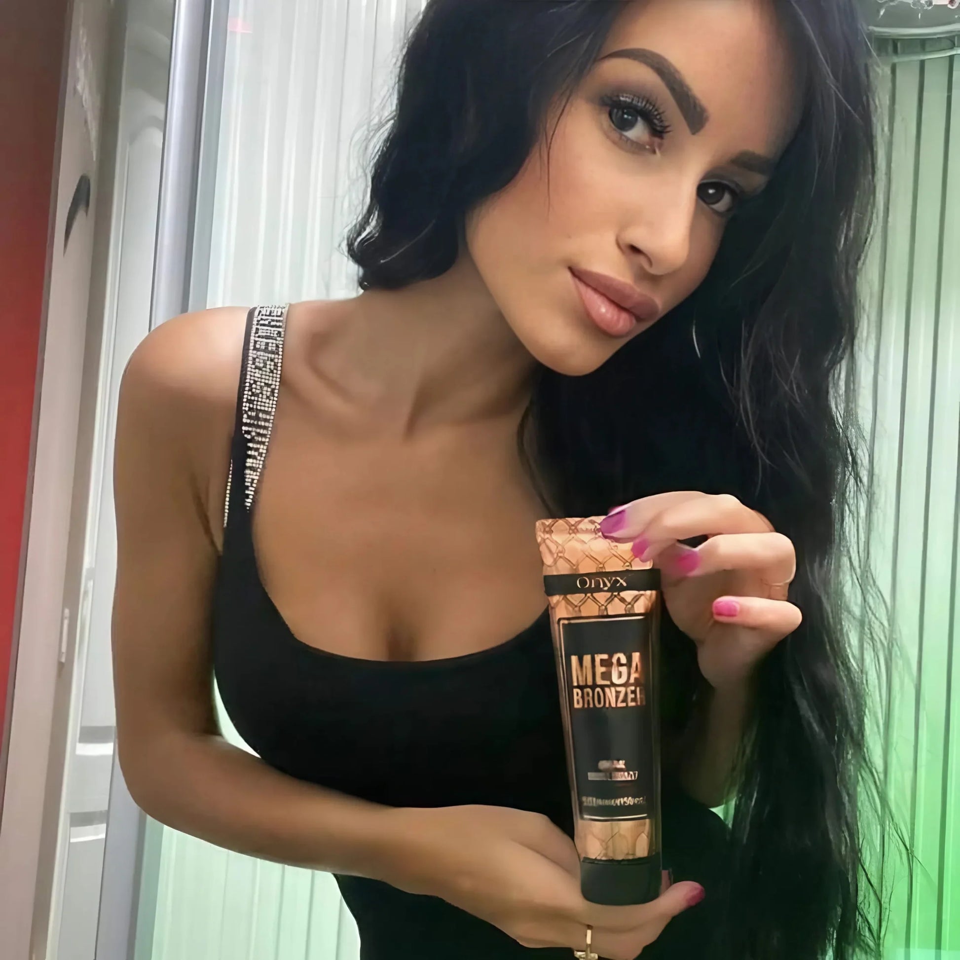 Brünette Frau mit eleganter Ausstrahlung präsentiert Onyx Mega Bronzer vor Solarium, ideal für eine tiefe und gleichmäßige Bräune