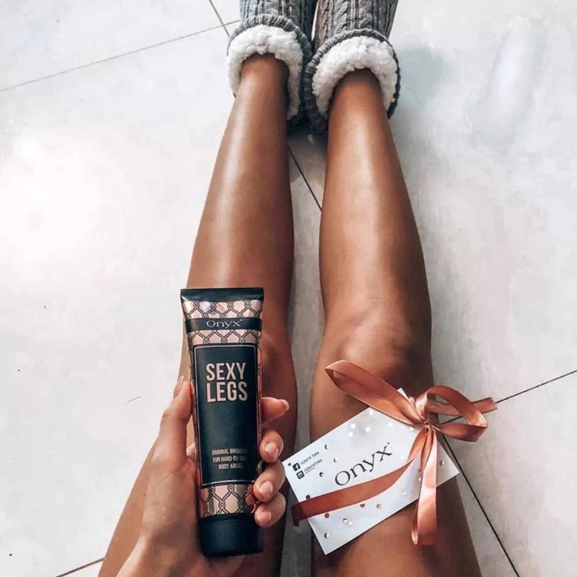 Onyx Sexy Legs Lotion neben Beinen mit Geschenkband und Karte auf dem Boden