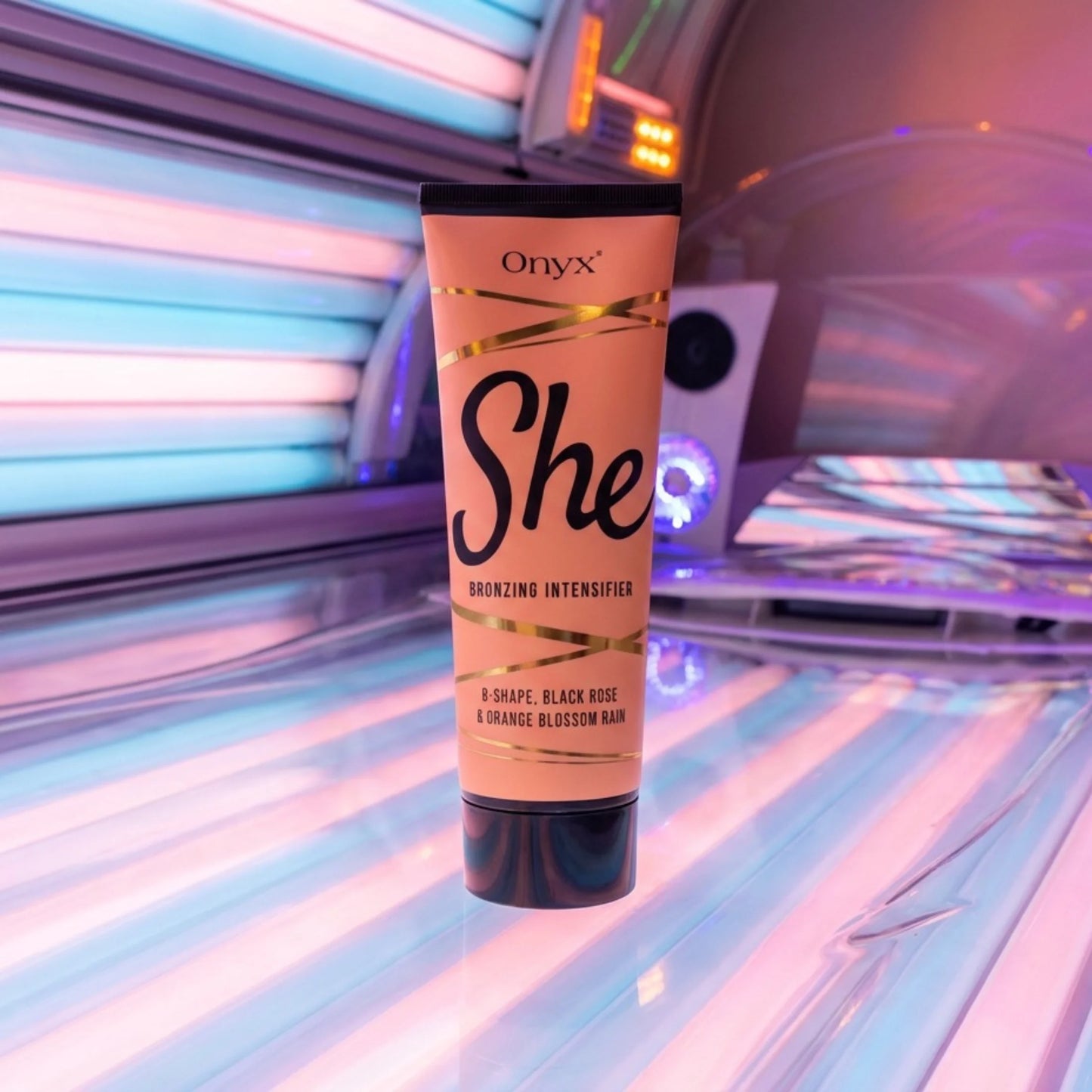 Die Tube Onyx She Bronzing Intensifier steht auf der Liegefläche eines Solariums. Die bunten Lichtleisten im Hintergrund setzen das Produkt in Szene.