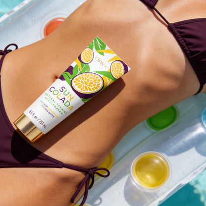 Die Tube Onyx Suncolada Natural Tanning Accelerator liegt auf dem Bauch einer Frau im dunkelvioletten Bikini auf einer aufblasbaren Liege im Wasser.