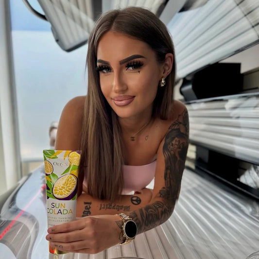 Eine Frau hält die Tube Onyx Suncolada Natural Tanning Accelerator in einer geöffneten Sonnenbank in die Kamera.
