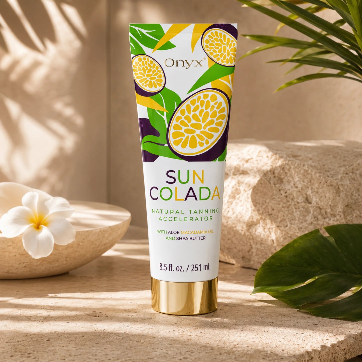 Die Tube Onyx Suncolada Natural Tanning Accelerator steht auf einer hellen Steinoberfläche neben tropischen Blättern, einer Blüte und dekorativen Schalen.