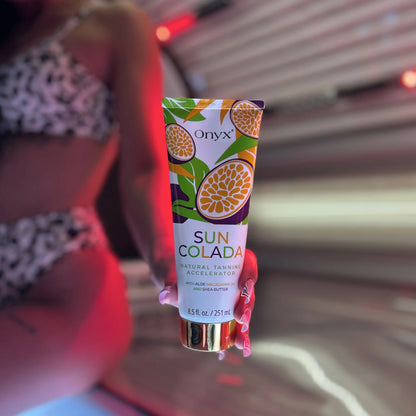 Eine Hand hält die Tube Onyx Suncolada Natural Tanning Accelerator vor einer geöffneten Sonnenbank mit roter Beleuchtung.