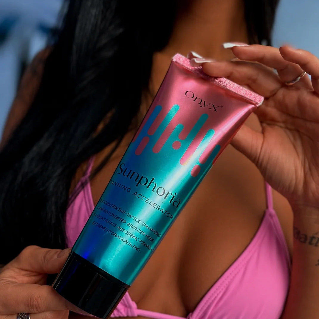 Nahaufnahme der metallisch rosa-blauen Tube Onyx Sunphoria Tanning Accelerator in den Händen einer Frau im rosa Bikini.
