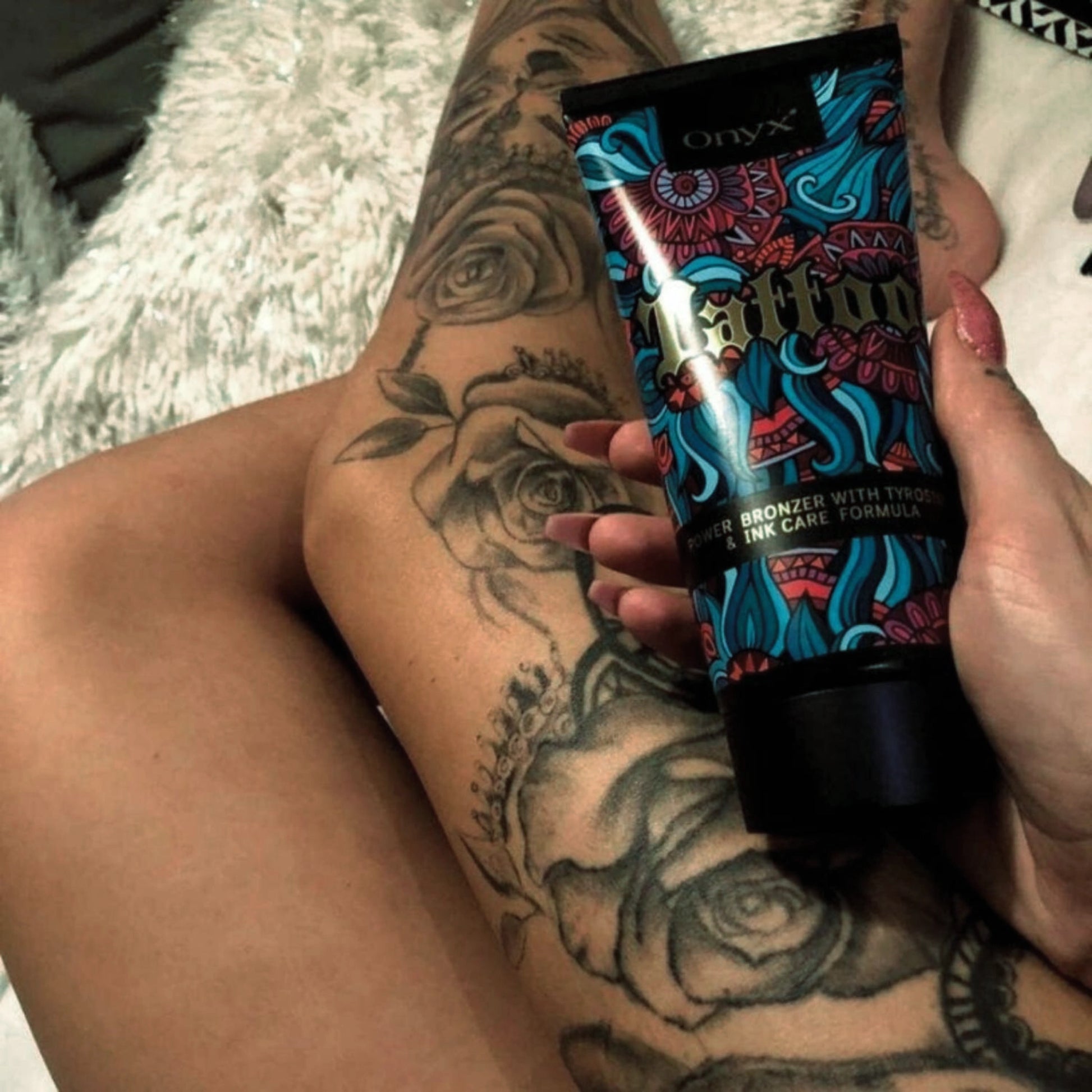 Onyx Tattoo Lotion in der Hand einer tätowierten Frau auf dem Bein, Tattoo-Pflege kombiniert mit intensiver Bräunung