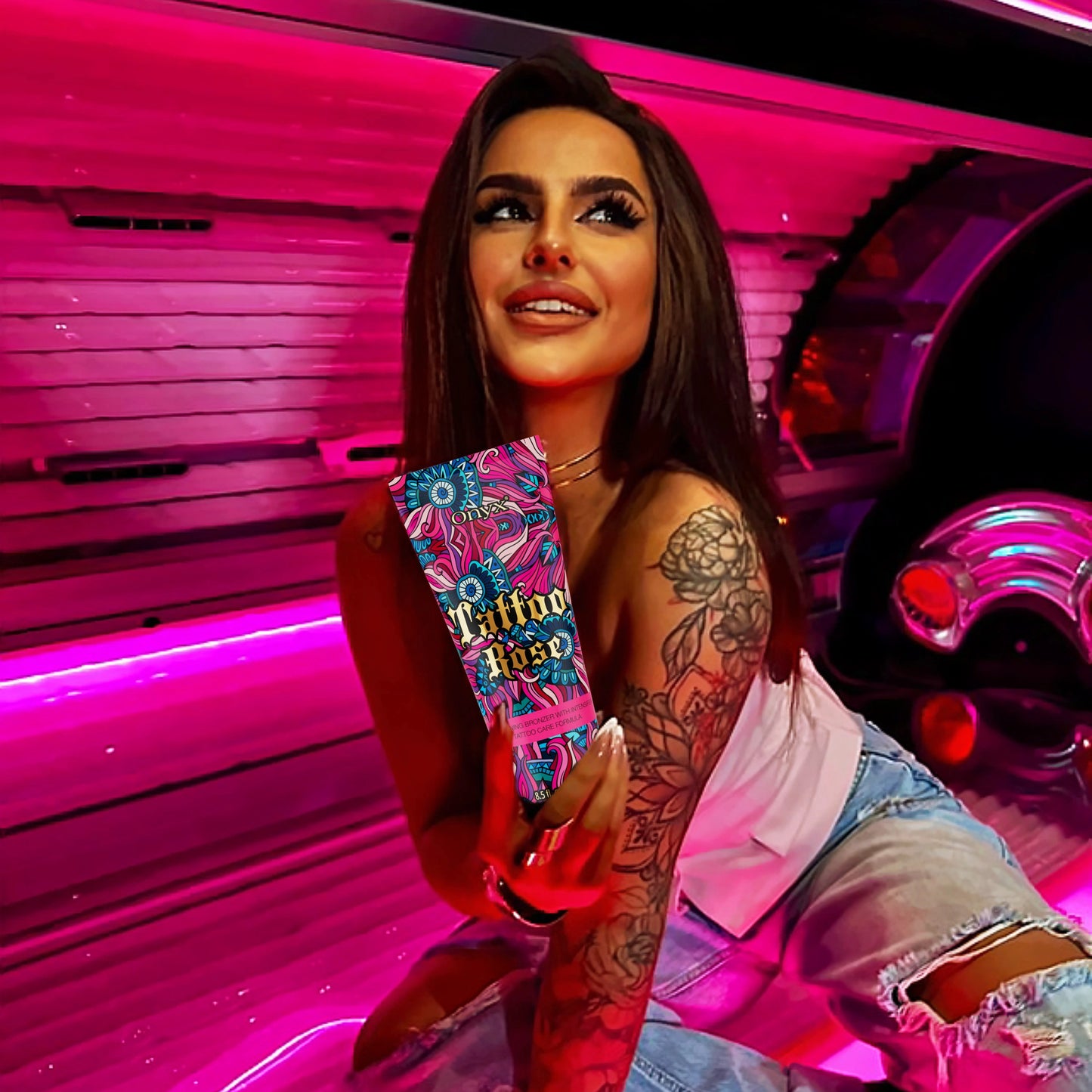 Lächelnde Frau mit Tattoos und langen Haaren hält Onyx Tattoo Rose Bräunungscreme in pink beleuchtetem Solarium