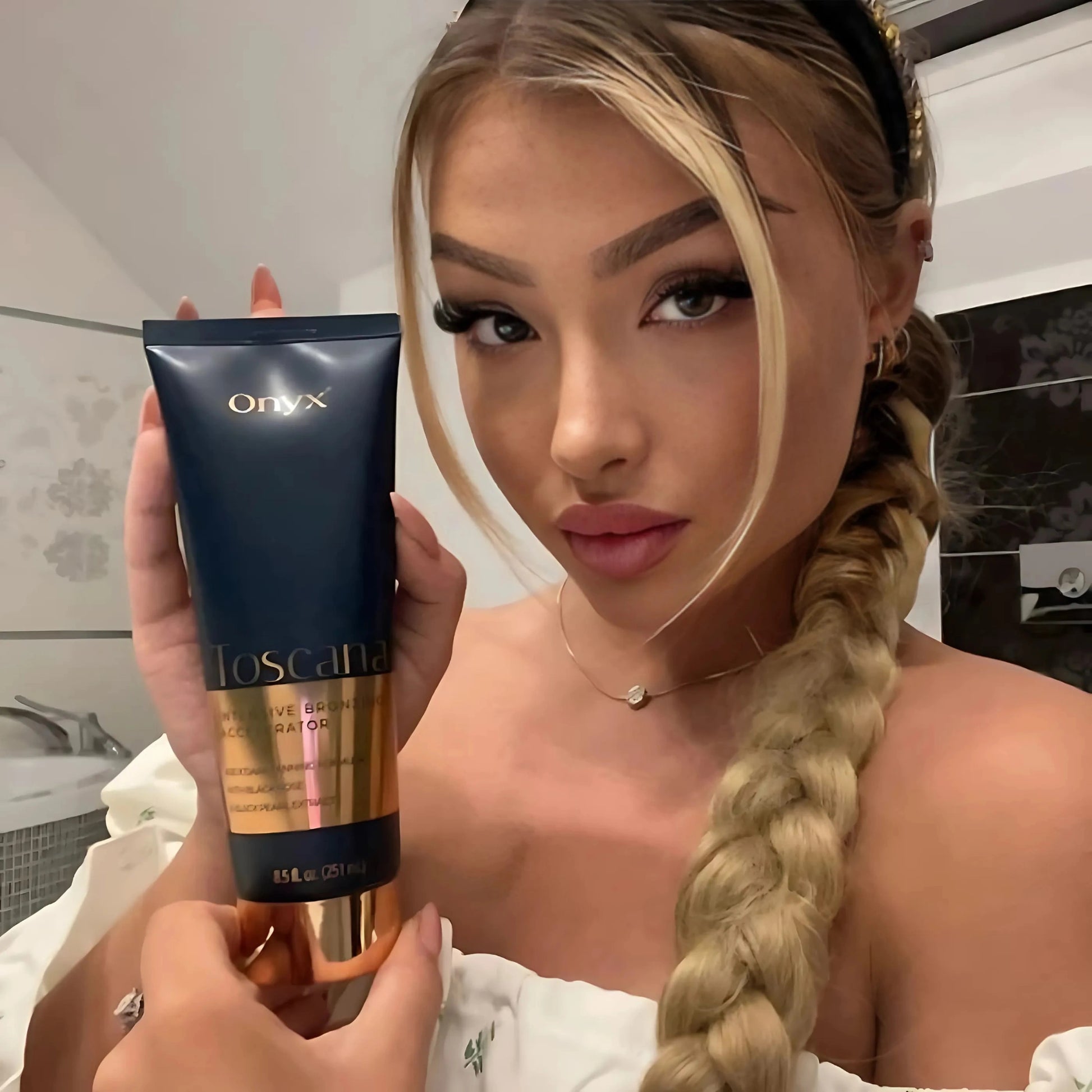 Blonde Frau mit Flechtfrisur hält Onyx Toscana Bräunungslotion in Badezimmerumgebung