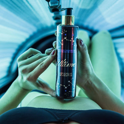 Frau mit lockigem Haar sitzt im weißen Badeanzug am Strand mit Blick auf das Meer, Onyx Ultime Lotion steht im Sand neben ihr